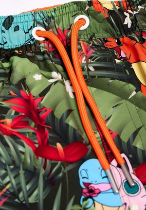 Grüne Badehorts mit tropischem Blumenmuster, ausgestattet mit orangen Kordelzügen und Ösen, die verschiedene Cartoonfiguren darstellen.