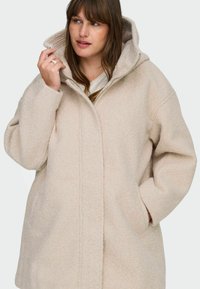 Beež oversize mantel pehmea, tekstuuriga kangaga. Omab kapuutsi, esiotste tõmblukk ja küljetaskud. Sile viimistlus minimaalsete õmblustega.