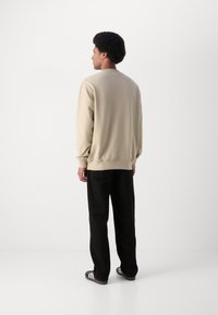 Felpa beige con maniche lunghe, collo a giro e polsini, abbinata a pantaloni neri larghi e scarpe nere con strisce bianche.