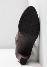 Zapato de ante gris con punta afilada y suela de goma negra texturizada, con el nombre de la marca "Tamaris" grabado en la parte inferior.