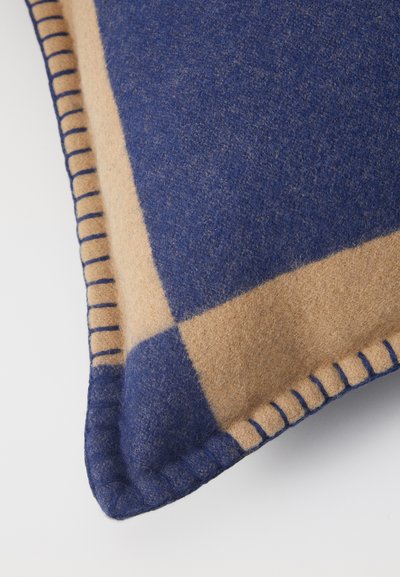 Wollen kussen met een blauw en beige ruitpatroon. Heeft een gestructureerde afwerking en contrasterende stiksels langs de randen voor extra detail.