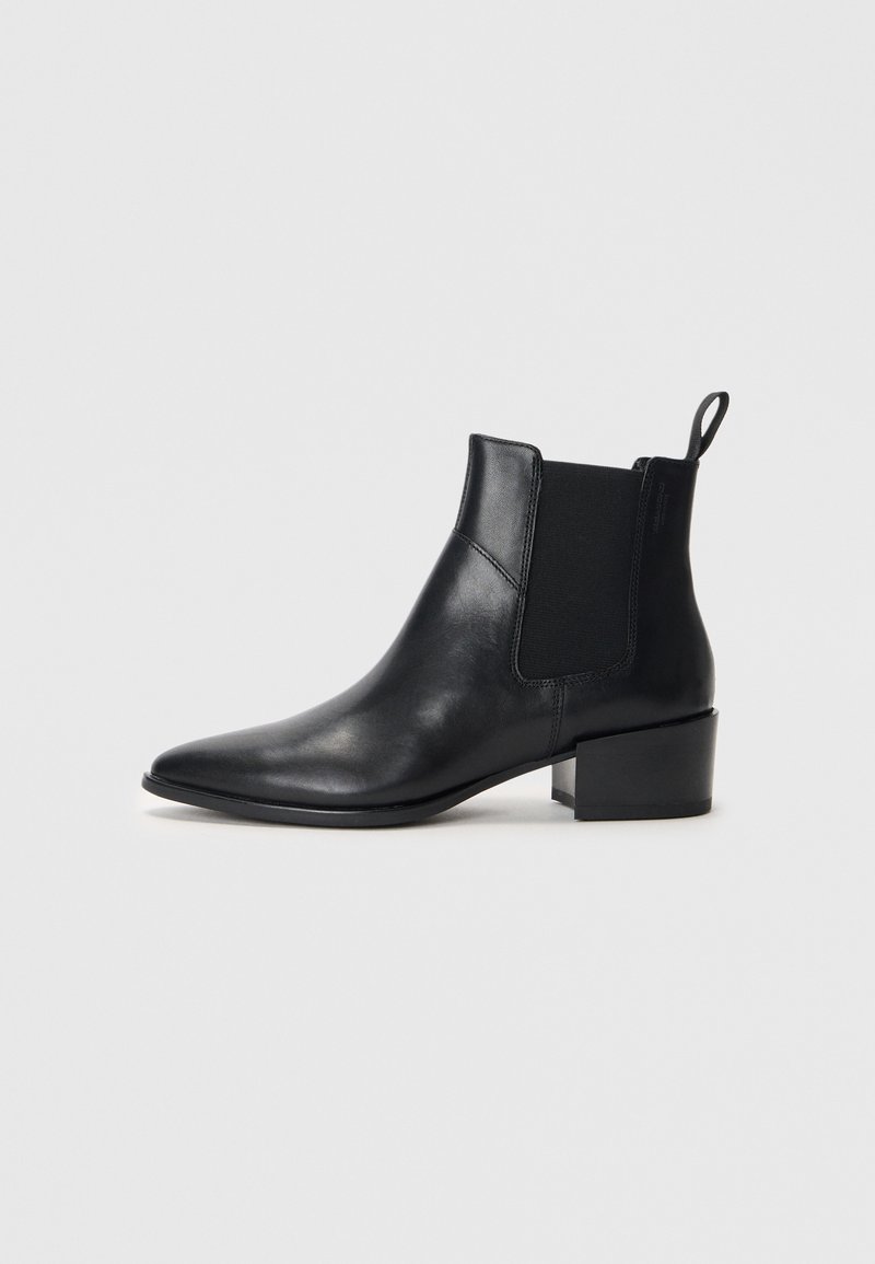 Bottine en cuir noir avec un bout pointu, des panneaux élastiques sur les côtés et un petit talon carré. Équipée d'une languette pour un enfilage facile.