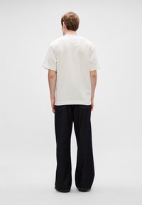 Λευκό βαμβακερό T-shirt και σκούρα μπλε φαρδιά τζιν παντελόνια, εμφανίζονται από πίσω, αναδεικνύοντας τη μαλακή υφή και την άνετη εφαρμογή.