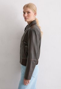 Bruine leren bomberjack met een ritssluiting aan de voorkant, geribde tailleband en zijzakken; heeft een gladde textuur en een klassiek kraagontwerp.