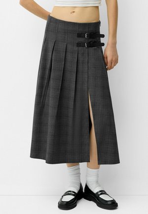 Jupe plissée grise taille haute avec deux boucles noires, fente latérale, portée avec des chaussettes blanches et des mocassins noir et blanc.