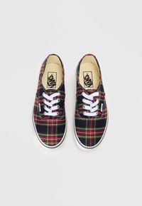 Încălțăminte din pânză cu un model tartan în nuanțe de roșu, galben și verde, având șireturi albe și tălpi din cauciuc. Logo-ul mărcii pe interiorul tălpii.