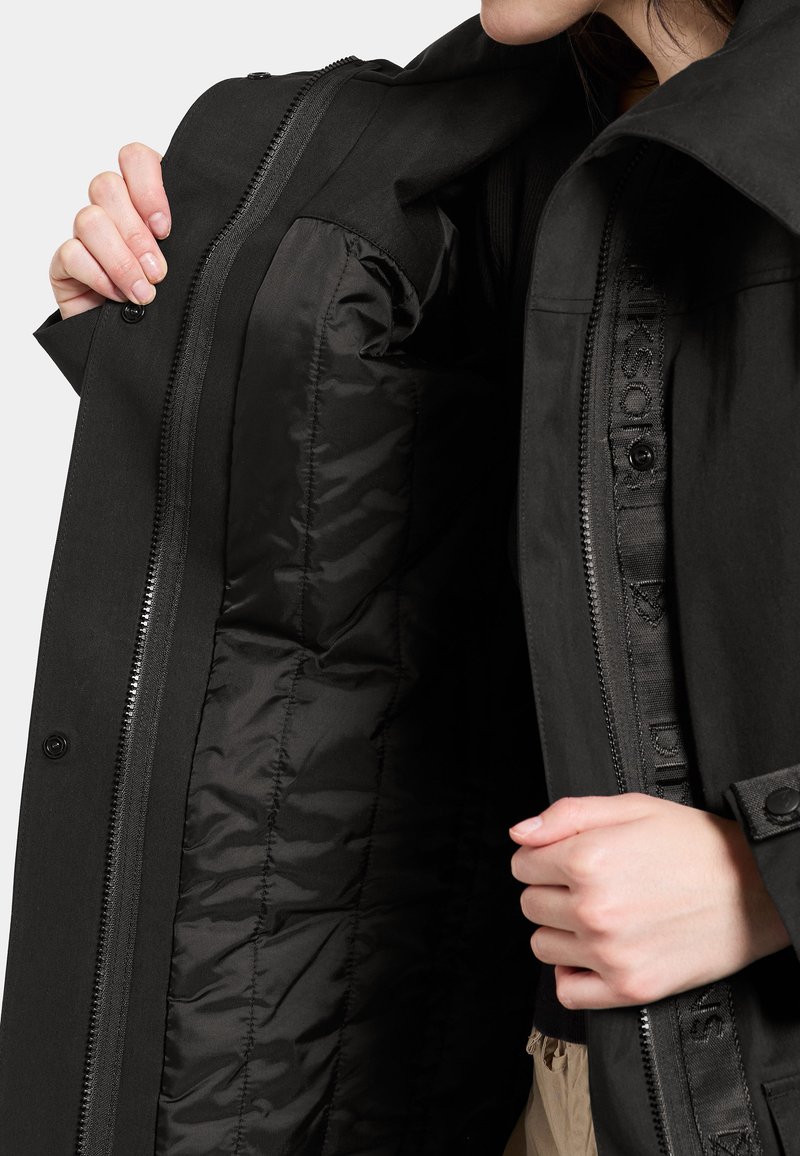 Schwarze Jacke mit glatter Außenseite und gestepptem Innenfutter. Verfügt über einen durchgängigen Reißverschluss und Knopfverschlüsse. Das Innenfutter ist ebenfalls schwarz.