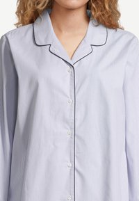 Vaaleansininen raidallinen pyjamasetti, jossa tumma pipingin koristus, pitkät hihat ja nappikiinnitys. Sisältää klassisen kauluksen ja hienovaraisen tekstuurin.