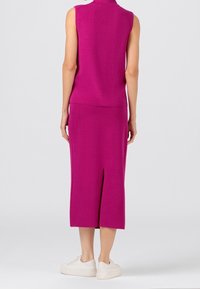 Fuchsia tvådelad outfit med en ärmlös topp och en knäslång kjol med en slid bak. Bärs med vita sneakers. Slät textur.