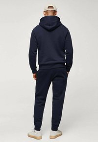 Felpa blu navy e pantaloni jogger coordinati realizzati in materiale morbido. Presenta un cappuccio regolabile, polsini elasticizzati e tasche laterali. Dallo stile casual e aderente.