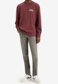 Vinröd långärmad tröja med vitt "Levi's"-märke, kombinerad med grå jeans och vita sneakers med svarta detaljer.