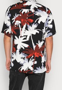 Camicia a maniche corte con sfondo nero, caratterizzata da grandi motivi floreali bianchi e rossi. Realizzata in tessuto leggero, ha una vestibilità comoda.
