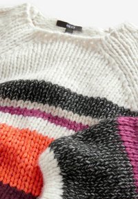 Gros plan d'un pull en tricot multicolore avec des rayures horizontales blanches, grises, roses, orange et bordeaux, affichant l'étiquette de la marque « NEXT ».