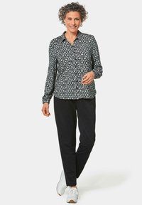 Zwart-witte geblokte overhemd met een kraag, gecombineerd met zwarte broek en witte sneakers. Kruidige haren en handen op de heupen.