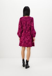 Robe mini à motif floral fuchsia avec de longues manches en ballon et une taille élastique, assortie à des bottines noires.