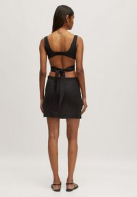 Zwart twee-delig set bestaande uit een crop top met een strik op de rug en een minirok met een gladde textuur, ontworpen in een aansluitende silhouette.