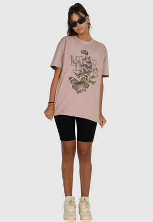 Rosa übergroßes T-Shirt mit einem Schmetterlingsgrafik und Text, kombiniert mit schwarzen figurbetonten Shorts und cremfarbenen Sneakern. Kurze Ärmel und eine lässige Passform.