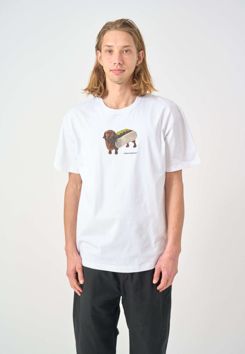 White cotton t-shirt featuring a colorful illustration of a dachshund with a hot dog. Short sleeves and relaxed fit. Black pants worn below.