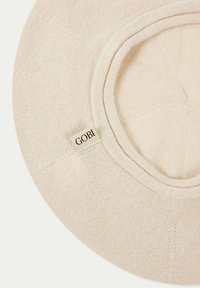 Beige virkade solhatt med en bred skärm, med en texturerad tyg och en liten vit etikett med "GOBI" i brunt.