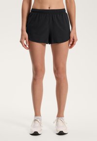 Čierne športové šortky s elastickým pásom, ľahký materiál a voľný strih. V kombinácii s bielymi teniskami s šedými detailmi.