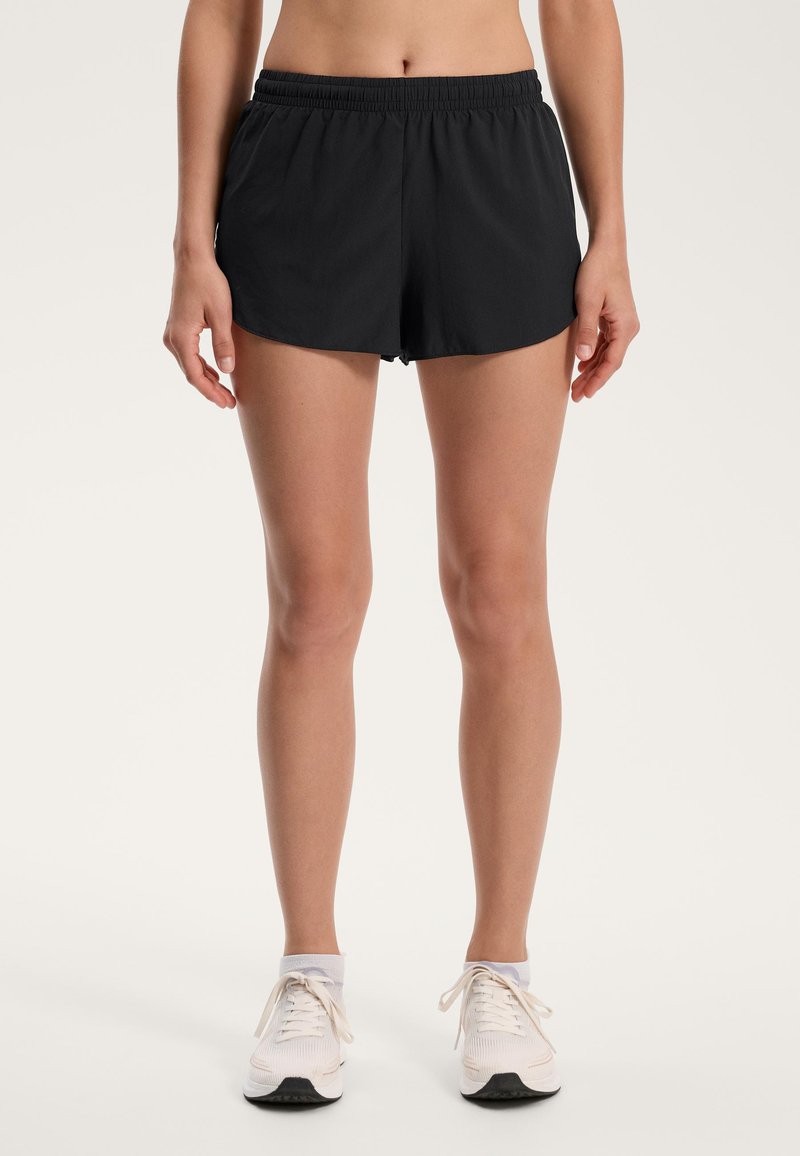 Čierne športové šortky s elastickým pásom, ľahký materiál a voľný strih. V kombinácii s bielymi teniskami s šedými detailmi.