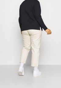 Maglione nero, jeans croppati beige chiaro con orli sfilacciati, sneakers bianche e calzini bianchi. Il modello è visto da dietro.