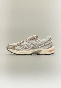 Zapatillas deportivas con parte superior de malla en crema y beige con detalles en blanco, puntera redonda, collar acolchado y suela de goma texturizada.