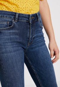 Mörkblå denimjeans med en figurnära design, som har fem fickor, subtila slitningar och kontrasterande sömmar vid midjan och sömmarna.
