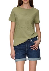 Olijfgroene T-shirt met korte mouwen en een lichtgroen grafisch ontwerp; gecombineerd met donkere denim shorts met omgeslagen zomen.