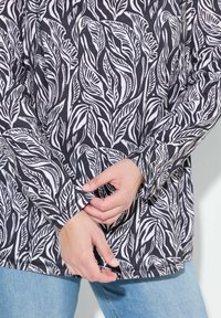 Haut à manches longues noir avec un motif de feuilles blanches. Caractérisé par une coupe décontractée, un ourlet arrondi et une couture simple le long des poignets et de l'encolure.