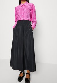 Blusa lunga a maniche corte plissettata di colore rosa con colletto, abbinata a una gonna lunga maxi in satin nero con tasche laterali e scarpe con plateau nere.