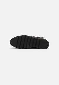 Baskets noires avec une semelle en caoutchouc texturé, présentant un motif strié pour une bonne adhérence, et des lacets plats. Design minimaliste sans logos visibles.