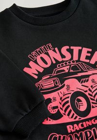Schwarzer Sweatshirt mit geripptem Rundhalsausschnitt und langen Ärmeln, mit einem leuchtend rosa Grafik eines Monstertrucks und detailliertem Text.