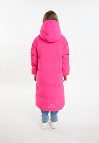 Lunga giacca piumino rosa con cappuccio, con segmenti trapuntati e polsini elastici. Abbinata a jeans di denim e sneaker bianche.