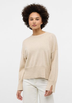 Beige gebreide trui met een ontspannen pasvorm, ronde halslijn en ribbelzoom. Beschikt over verlaagde schouders en zijsplitten bij de manchetten voor extra detail.