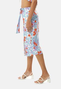 Floral midi skirt in light blue, featuring red and purple patterns, tied at the waist. Worn with white heeled sandals.
