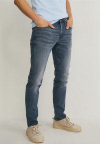 Slim-fit blå denimjeans med förslitning, fem fickor och en traditionell gylf. Matchas med ljusa sneakers.