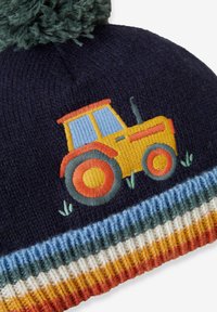 Narzutka dziergana w kolorze granatowym z kolorową haftowaną traktorową aplikacją. Posiada teksturowany, w paski mankiet w kolorze niebieskim, pomarańczowym i żółtym, zwieńczony zielonym pomponem.