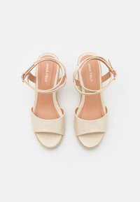 Beige plattform sandaler med en glatt lær overdel, åpen tå og tynne ankelstropper. Har en naturlig teksturert kilehæl.