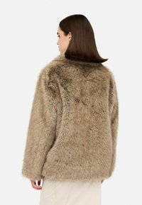 Cappotto in pelliccia sintetica color marrone chiaro con una texture spessa e morbida. Presenta una vestibilità rilassata e maniche ampie, con una leggera lucentezza su tutta la superficie.