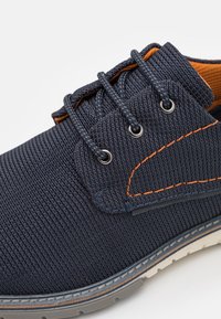 Chaussure textile décontractée bleu marine avec des accents orange, dotée de lacets ronds, d'œillets argentés, d'une surface texturée et d'une semelle en caoutchouc.
