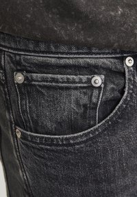 Vaqueros de mezclilla negra con un acabado desgastado, que cuentan con un bolsillo delantero con un detalle de botón plateado y una tela texturizada.