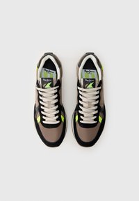 Tenisky s čiernym a hnedým vrchom, s módnymi zelenými akcentmi, textúrovanou podrážkou a béžovými šnúrkami. Logo viditeľné na jazyku.