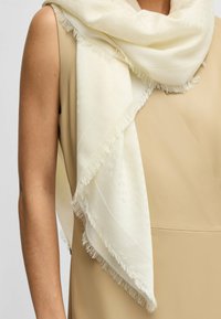 Light ivory scarf with fringed edges, draped over a neutral-colored top. Smooth texture with subtle pattern details.
