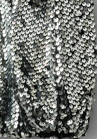 Sølvfarvet palietstof med cirkulære paletter på en sort baggrund, der viser en skimrende tekstur og et lagdelt draperedesign.