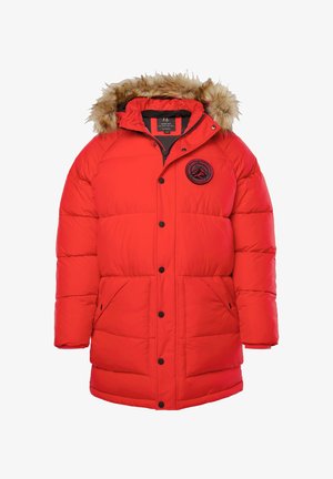 Rød polstret vinterjakke med hætte med pelskant, foran trykknapper, sidelommer og et sort cirkulært mærke på brystet.