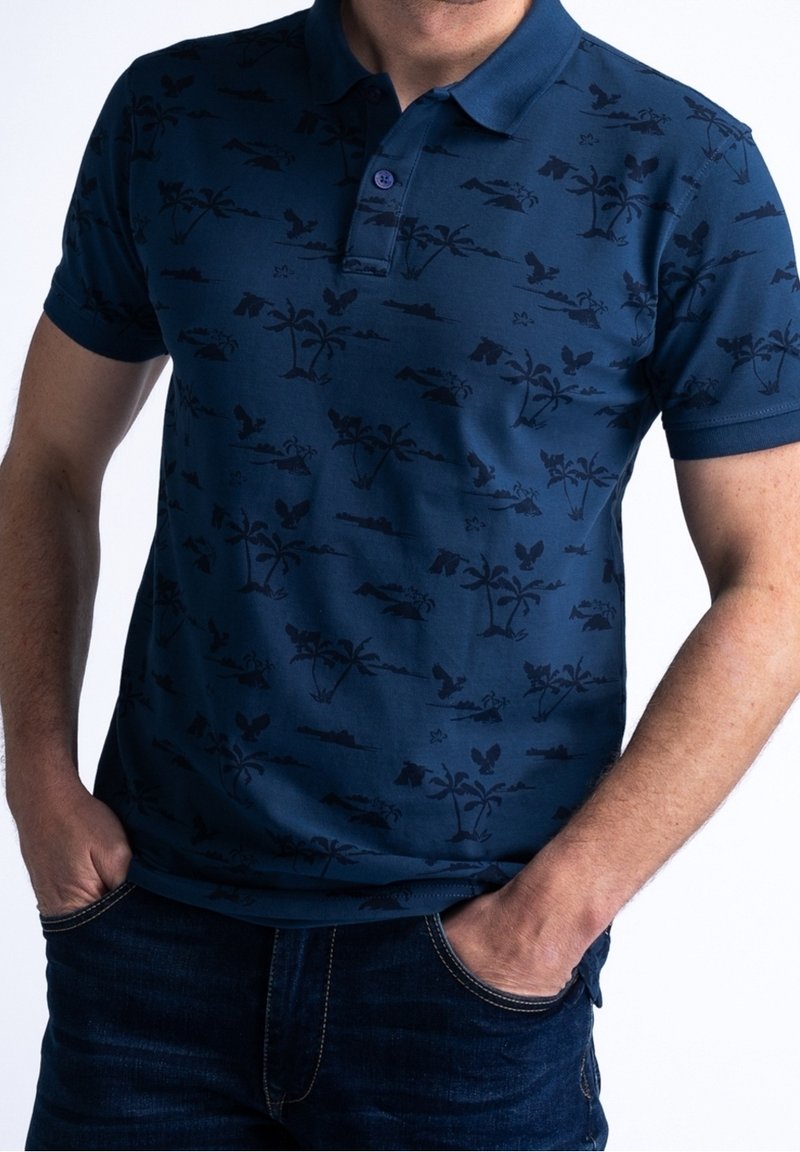 Mörkblå pikétröja med ett mönster av mörka palmträd och landskap. Har krage, korta ärmar och en knappslå med en knapp.