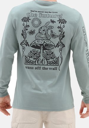 Langärmliges hellblaues Hemd mit einem schwarzen Grafikdesign, das einen Hasen, Pilze und florale Elemente zeigt. Der aufgedruckte Text lautet: "Du bist nie zu weit von der Zukunft entfernt!"