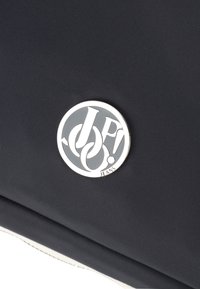 Borsa in tessuto nero con una texture, dotata di un accento logo rotondo in argento con "JP!" e "JEANS" incisi, posizionato in modo prominente sulla superficie.