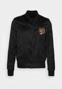 Veste bomber en satin noir avec col, poignets et bas côtelés, ornée d'une tête de tigre rugissante brodée sur la poitrine gauche.